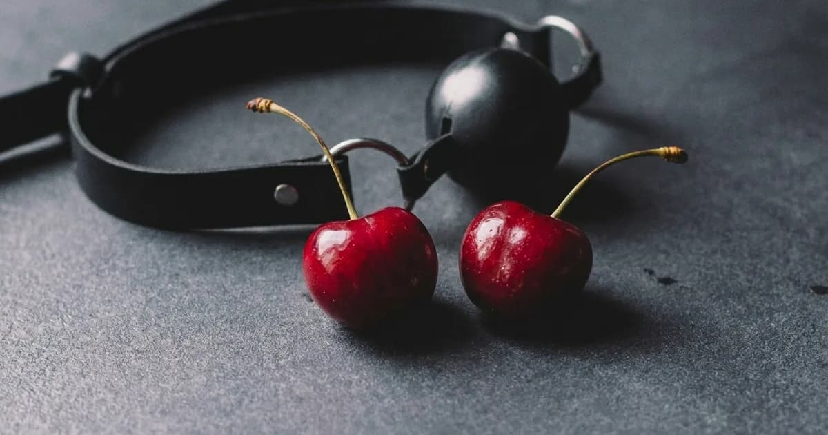 Cherries in front of a black ball gag.